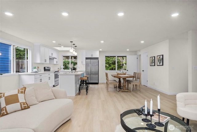 living area with baseboards, recessed lighting, and light wood-style floors