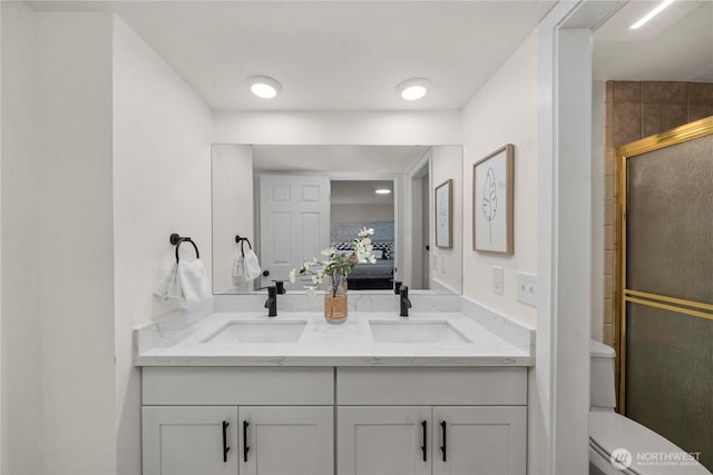 ensuite bathroom featuring double vanity, connected bathroom, a sink, and a shower with shower door