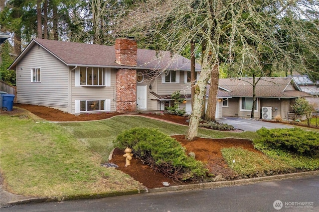 bi-level home with aphalt driveway, a front yard, a shingled roof, and a chimney