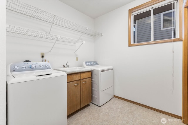 washroom featuring cabinet space, baseboards, a sink, and washing machine and clothes dryer