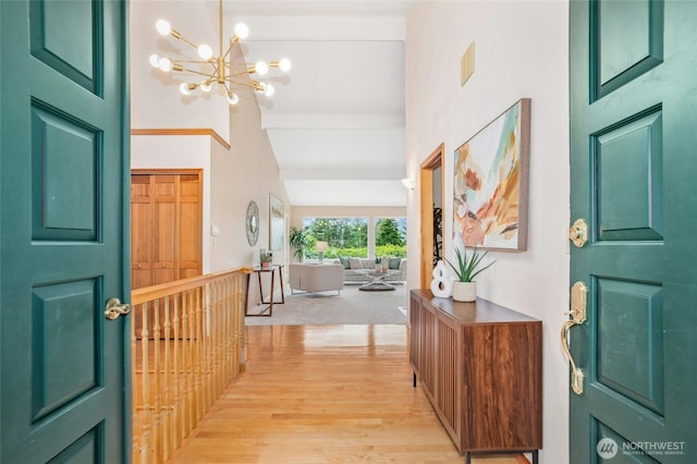 entryway featuring light wood-style flooring, beamed ceiling, an inviting chandelier, and a towering ceiling