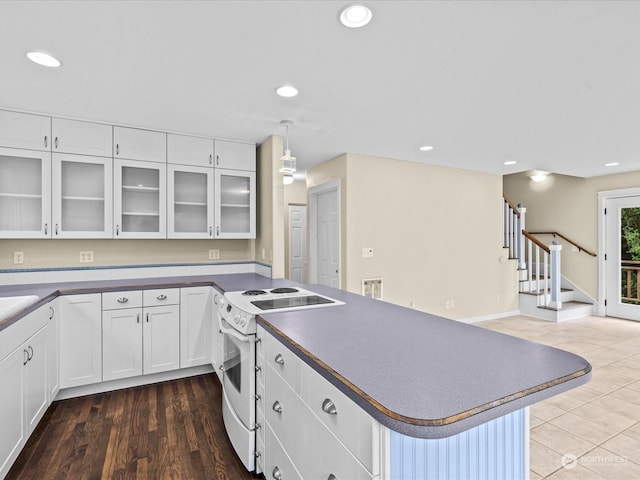 kitchen featuring white electric stove, white cabinets, a kitchen breakfast bar, hanging light fixtures, and dark wood-type flooring