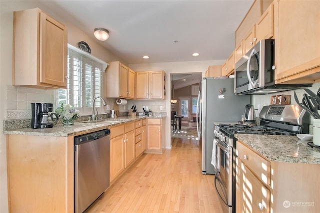 kitchen with sink, stainless steel appliances, light stone countertops, light brown cabinets, and light wood-type flooring