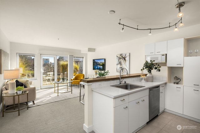 kitchen featuring stainless steel dishwasher, kitchen peninsula, sink, and white cabinets