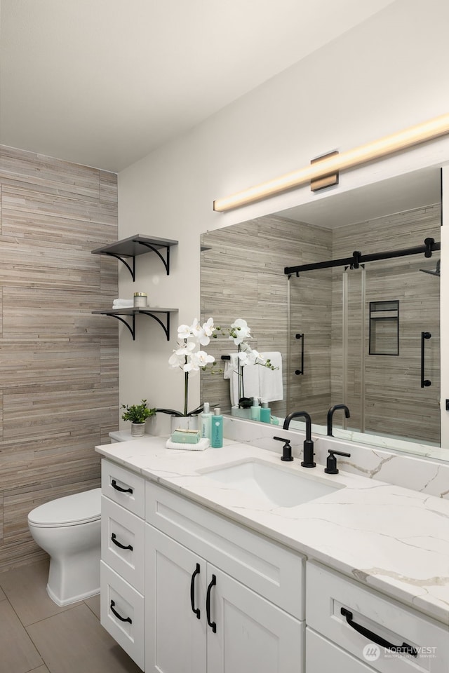 bathroom featuring a shower with door, vanity, tile walls, and toilet