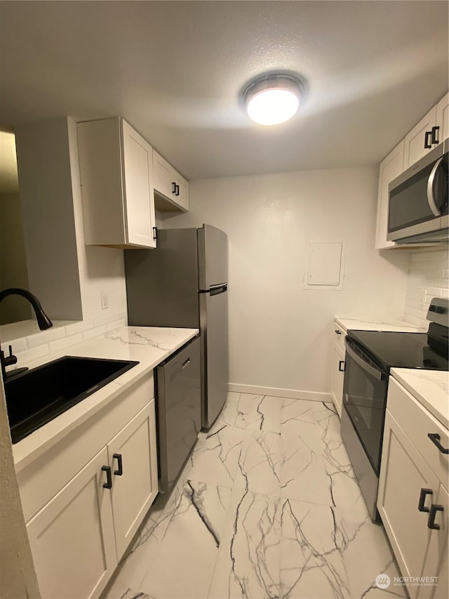 kitchen featuring sink, appliances with stainless steel finishes, white cabinetry, tasteful backsplash, and light stone countertops