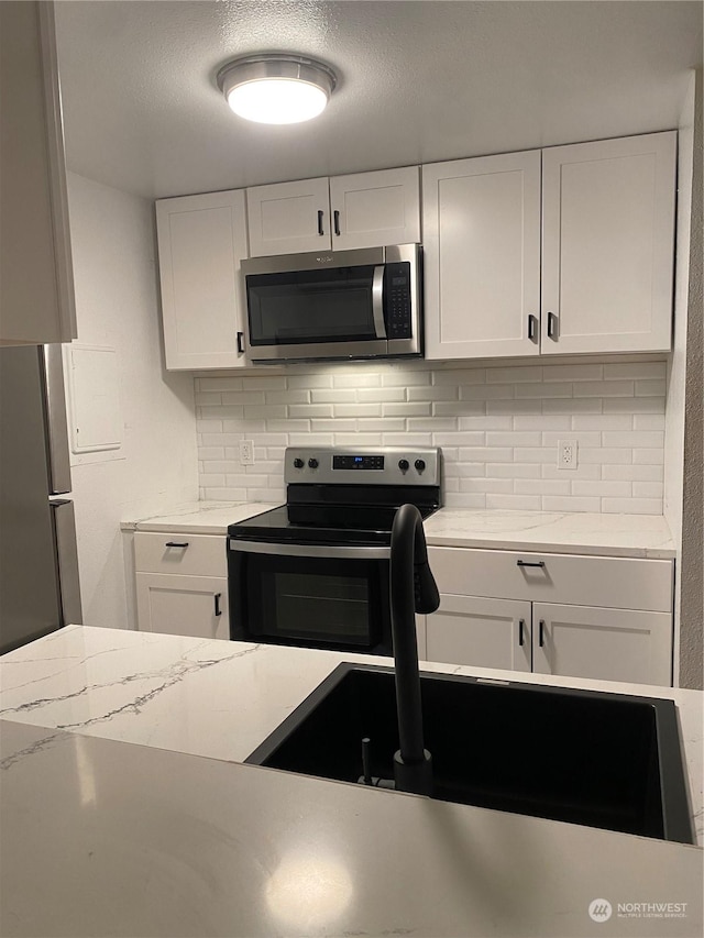 kitchen with appliances with stainless steel finishes, white cabinetry, light stone counters, a textured ceiling, and decorative backsplash