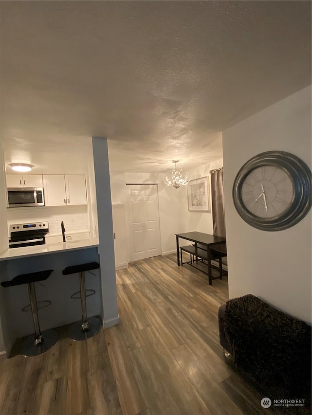 interior space with dark wood-type flooring, appliances with stainless steel finishes, white cabinets, pendant lighting, and backsplash