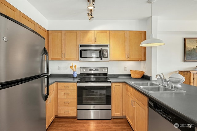 kitchen featuring stainless steel appliances, dark countertops, hanging light fixtures, and a sink