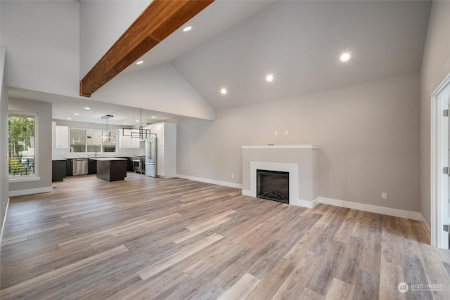 unfurnished living room with beamed ceiling, high vaulted ceiling, and light hardwood / wood-style floors