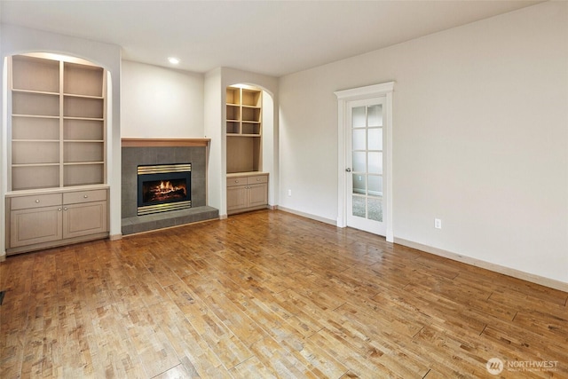 unfurnished living room with a tile fireplace, wood-type flooring, and built in shelves