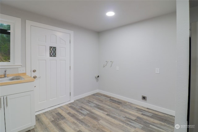 clothes washing area with cabinets, hookup for an electric dryer, sink, and light wood-type flooring