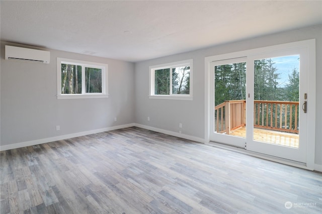 unfurnished room with a wall mounted air conditioner, a textured ceiling, and light hardwood / wood-style flooring