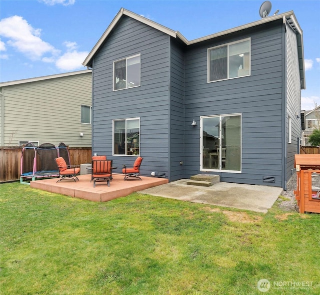 rear view of property featuring fence, a trampoline, a patio area, and a yard