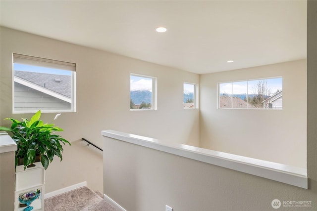 corridor featuring a wealth of natural light, an upstairs landing, carpet flooring, and baseboards