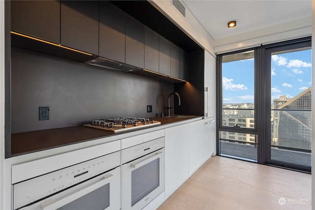 kitchen with stainless steel gas stovetop, sink, oven, and light hardwood / wood-style floors