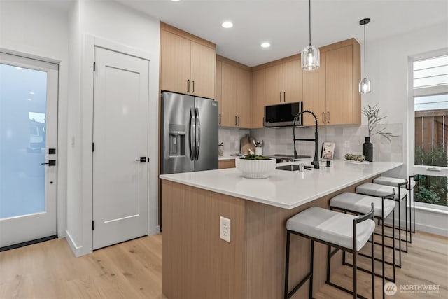 kitchen featuring pendant lighting, stainless steel appliances, light countertops, light brown cabinets, and a peninsula