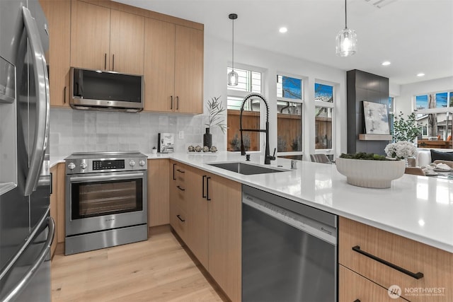 kitchen featuring stainless steel appliances, light countertops, a sink, and hanging light fixtures