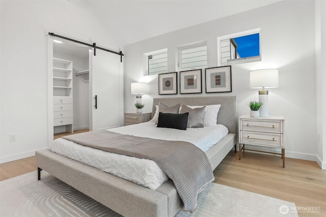 bedroom featuring a barn door, a walk in closet, light wood-style flooring, and baseboards