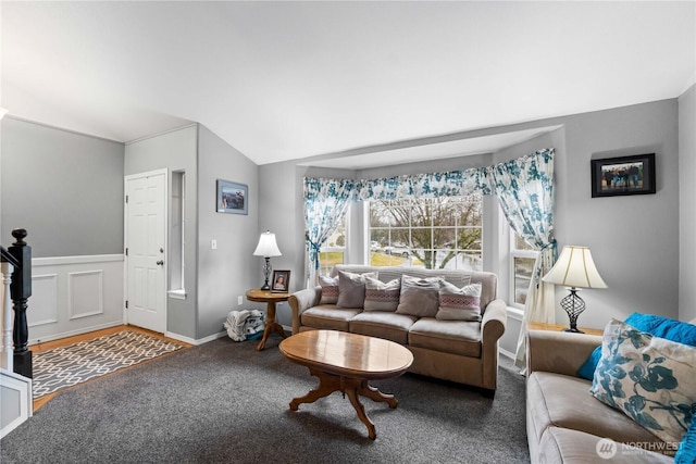 living area featuring carpet, wainscoting, vaulted ceiling, and a decorative wall