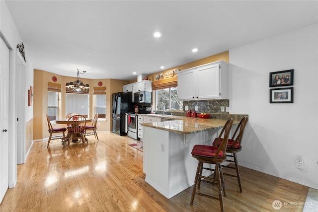 kitchen with stainless steel appliances, a sink, light wood-style flooring, and decorative backsplash