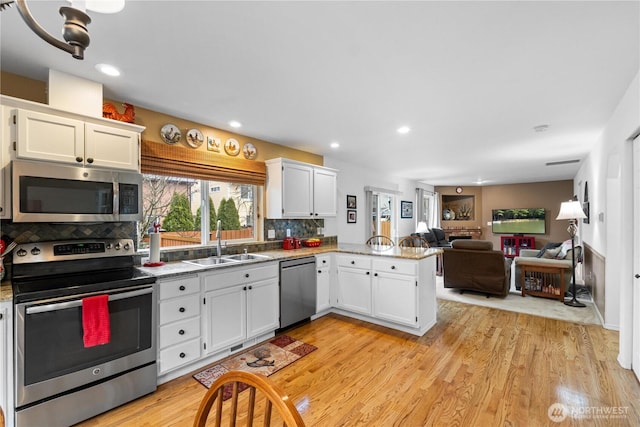 kitchen with appliances with stainless steel finishes, white cabinetry, a sink, light wood-type flooring, and a peninsula