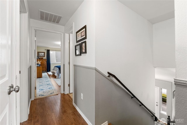 hallway with baseboards, visible vents, wood finished floors, and an upstairs landing