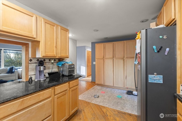 kitchen with dark stone countertops, light brown cabinets, light wood-style flooring, freestanding refrigerator, and tasteful backsplash