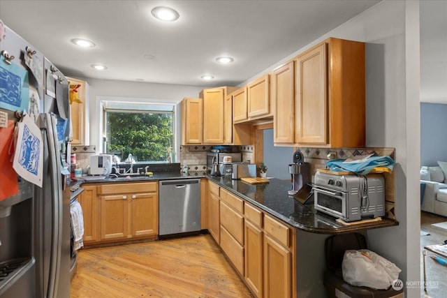 kitchen with light wood finished floors, dark stone counters, decorative backsplash, appliances with stainless steel finishes, and a sink