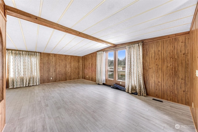 spare room featuring wooden walls, vaulted ceiling with beams, a textured ceiling, and light hardwood / wood-style floors