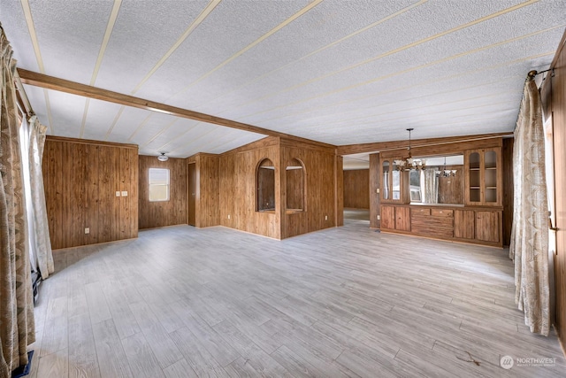 unfurnished living room with a notable chandelier, wood-type flooring, wooden walls, and a textured ceiling