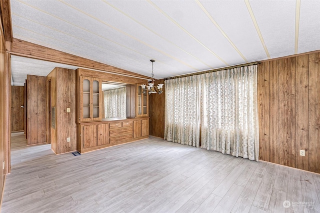 unfurnished dining area with a notable chandelier, light hardwood / wood-style floors, and wood walls