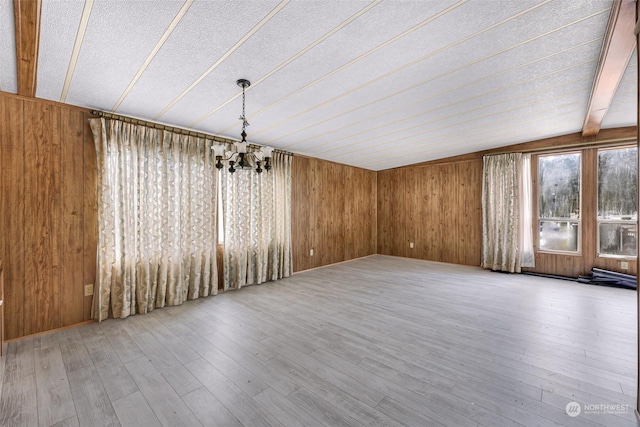 interior space with a textured ceiling, wooden walls, a notable chandelier, hardwood / wood-style flooring, and beam ceiling