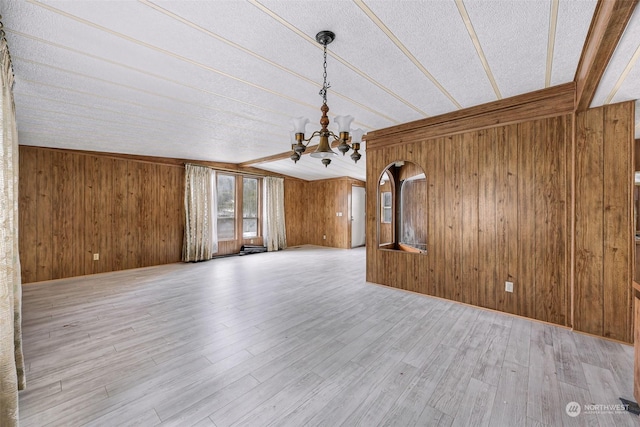 unfurnished living room with a notable chandelier, wooden walls, and light hardwood / wood-style floors