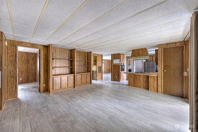 unfurnished living room featuring light hardwood / wood-style floors, a textured ceiling, and wood walls