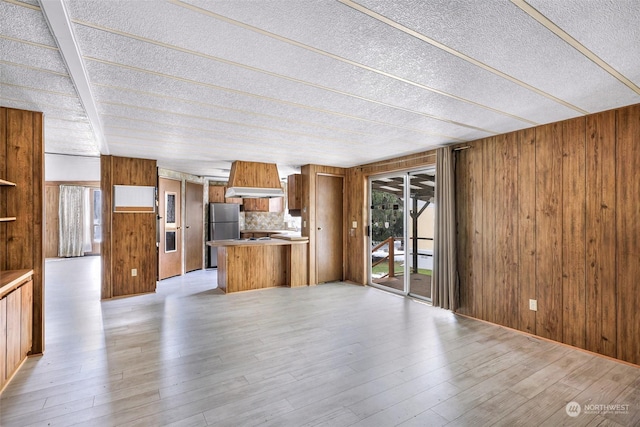 unfurnished living room with light hardwood / wood-style floors, a textured ceiling, and wood walls