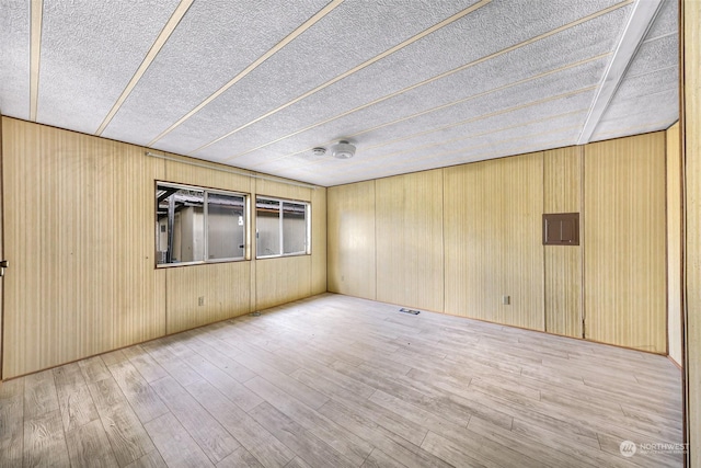 spare room featuring electric panel, light hardwood / wood-style floors, and a textured ceiling