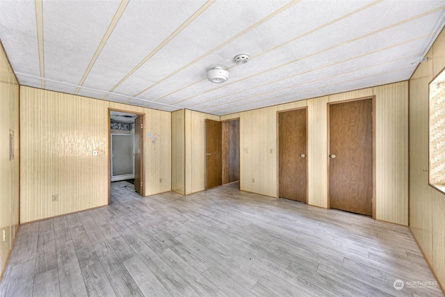 unfurnished bedroom with multiple closets, wood walls, and light hardwood / wood-style flooring