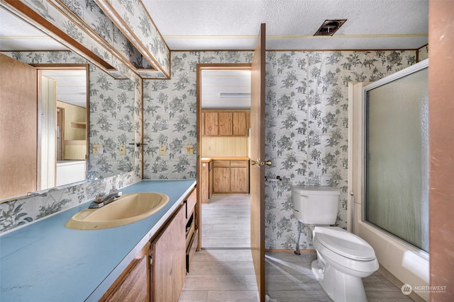 full bathroom featuring bath / shower combo with glass door, vanity, toilet, and a textured ceiling