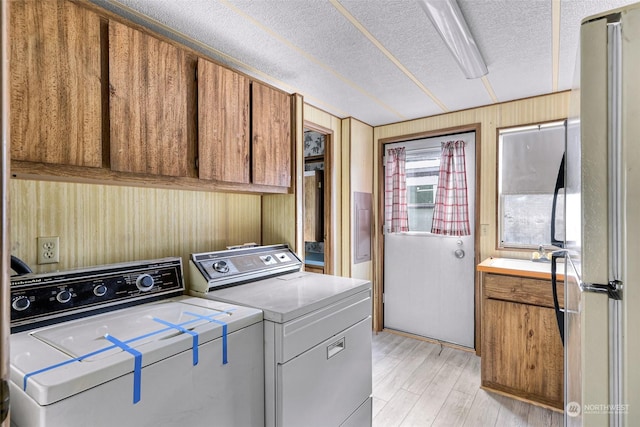 laundry room with cabinets, a textured ceiling, wooden walls, washer and clothes dryer, and light hardwood / wood-style floors