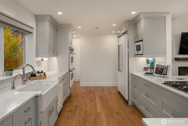 kitchen with built in appliances, sink, backsplash, and light wood-type flooring