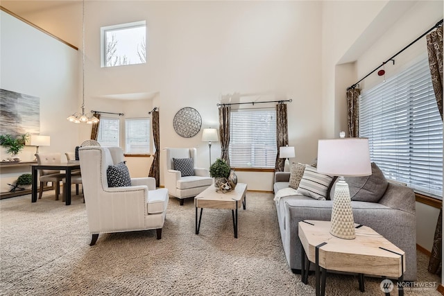 carpeted living area with a chandelier, a towering ceiling, and baseboards