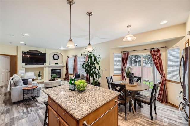 kitchen with pendant lighting, brown cabinetry, freestanding refrigerator, open floor plan, and a kitchen island