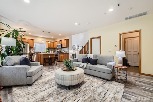 living area featuring light wood finished floors, baseboards, visible vents, stairway, and recessed lighting