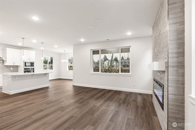 unfurnished living room with a large fireplace, a chandelier, and dark hardwood / wood-style flooring