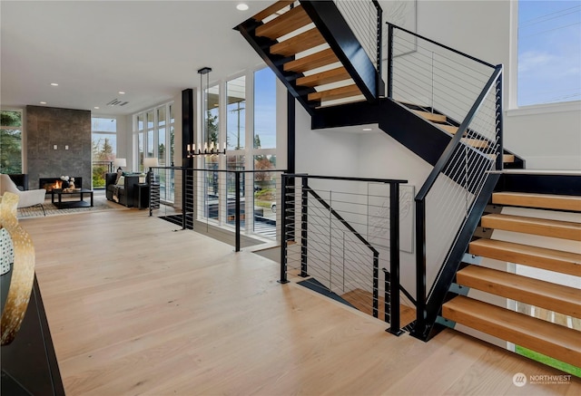 staircase with a large fireplace, floor to ceiling windows, and wood-type flooring