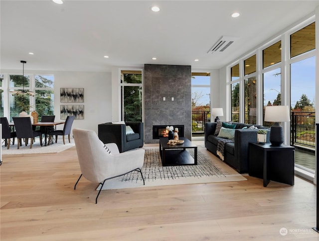 living room featuring a tile fireplace, a healthy amount of sunlight, light hardwood / wood-style floors, and a wall of windows