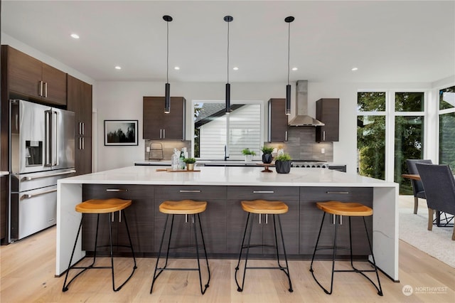 kitchen with wall chimney range hood, a breakfast bar area, high end refrigerator, and a center island with sink