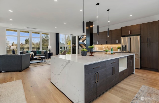 kitchen with high end refrigerator, dark brown cabinets, hanging light fixtures, light hardwood / wood-style flooring, and a large island