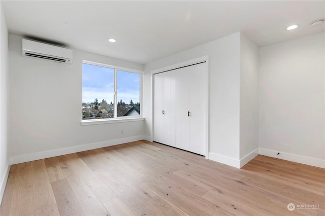 unfurnished bedroom featuring a closet, light hardwood / wood-style floors, and an AC wall unit